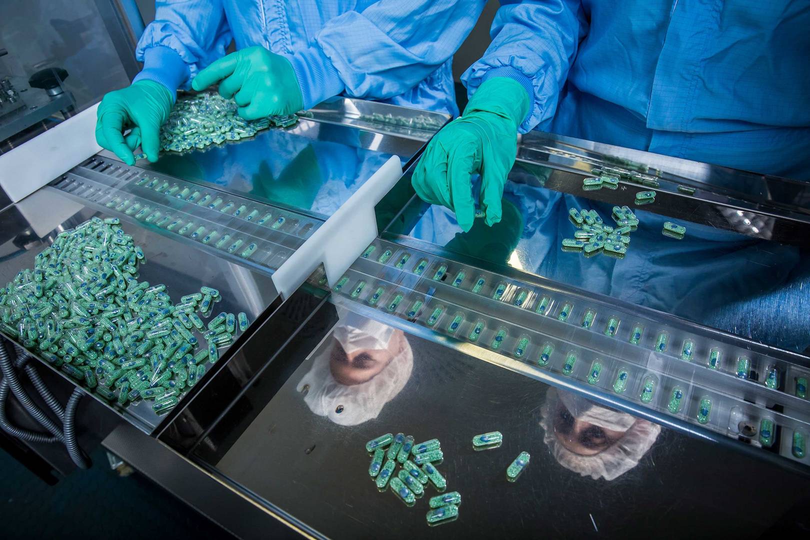 Two operators placing capsules on the tray of a blistering machine