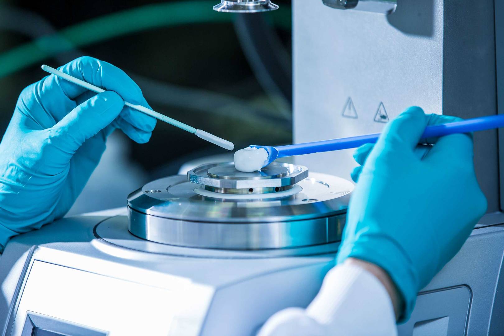 Gloved hands of a scientist preparing a sample on laboratory equipment for analysis