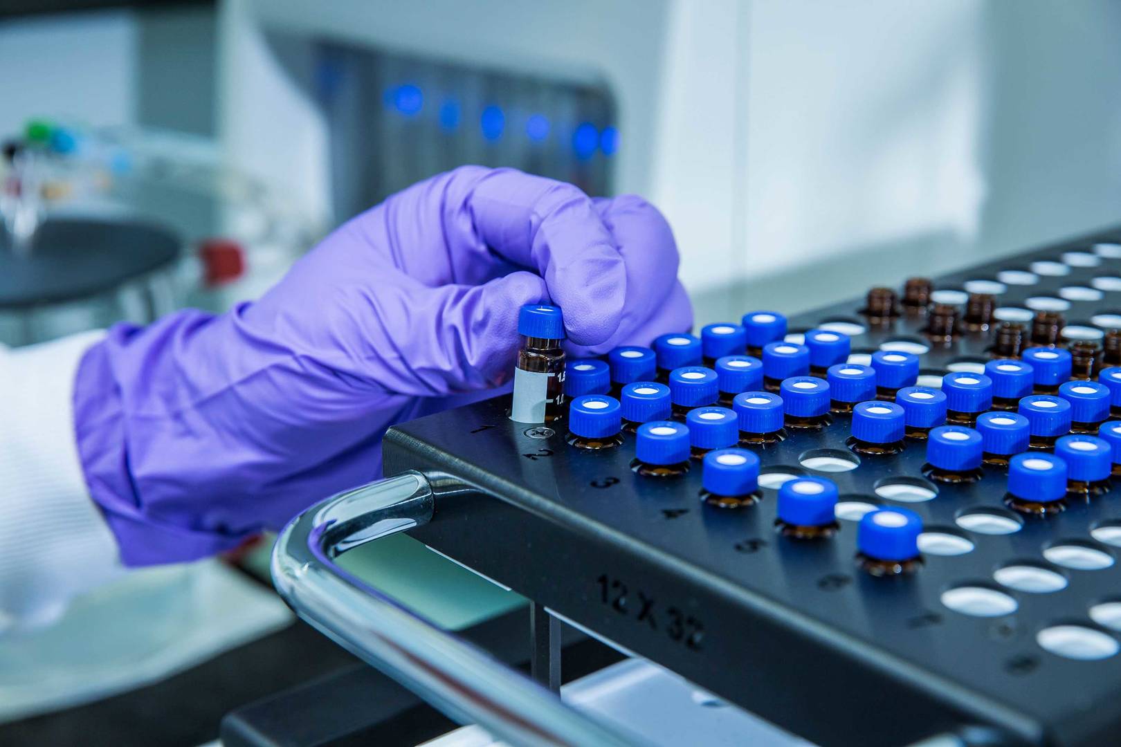 Hand with purple gloves in front of the plate where HPLC vials are displayed