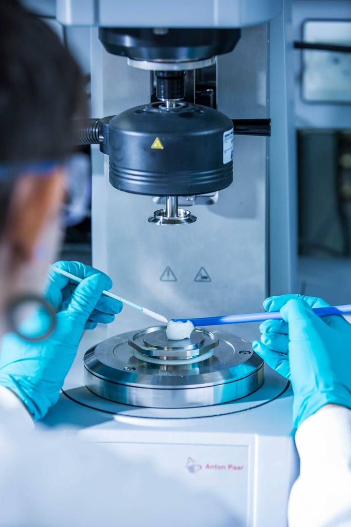 A lab technician wearing safety glasses and teal gloves uses an Anton Paar rheometer to analyze a sample
