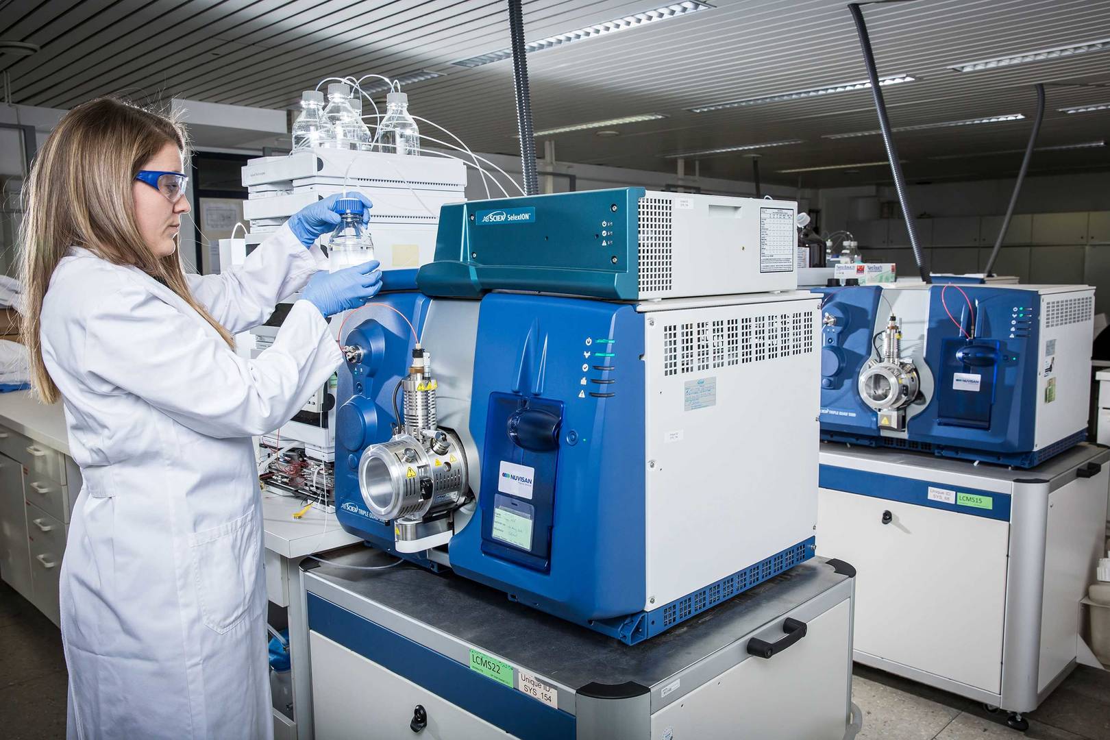 A laboratory technician holds the solvent bottle next to a mass spectrometer