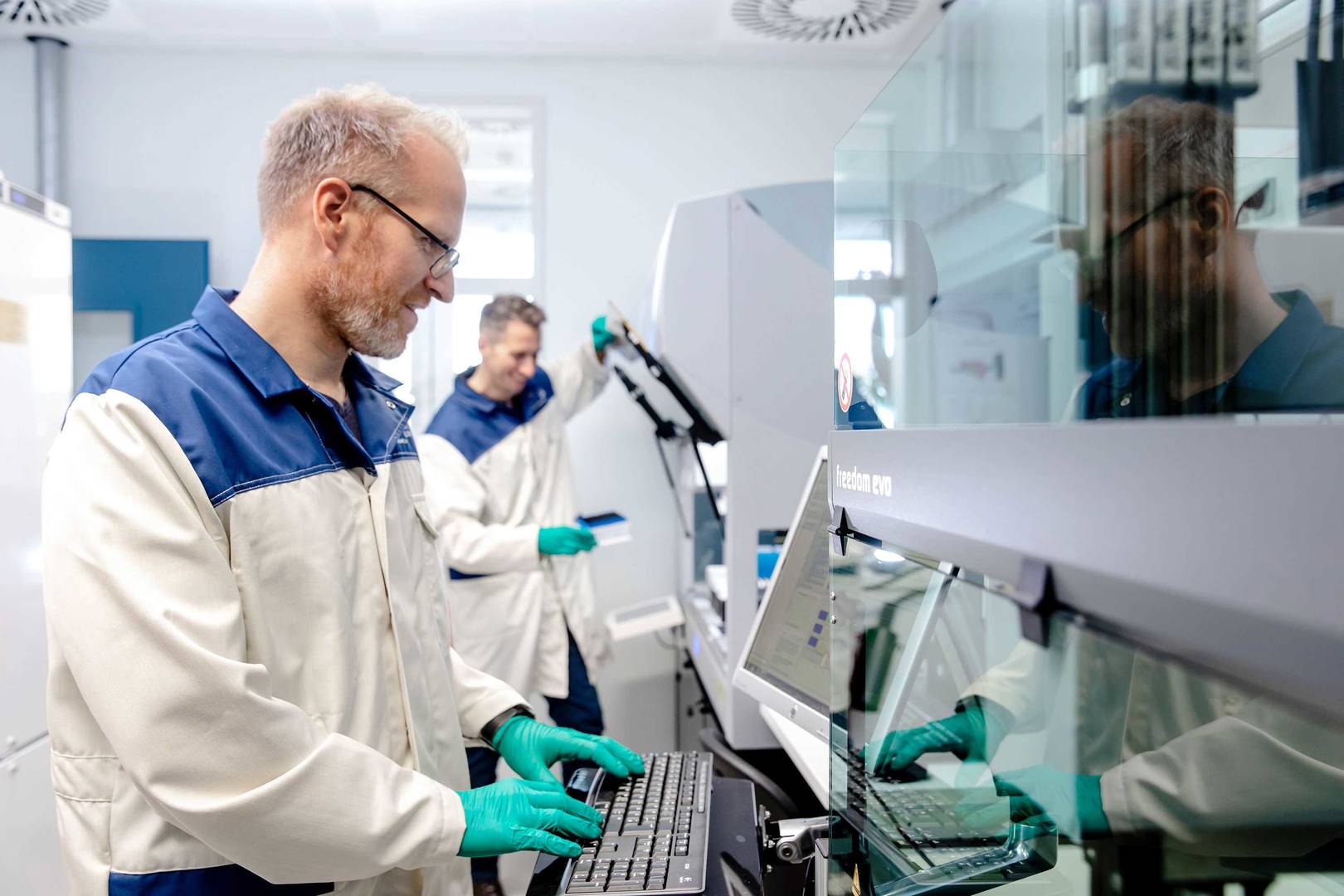 Two scientists operating large liquid handling machines 