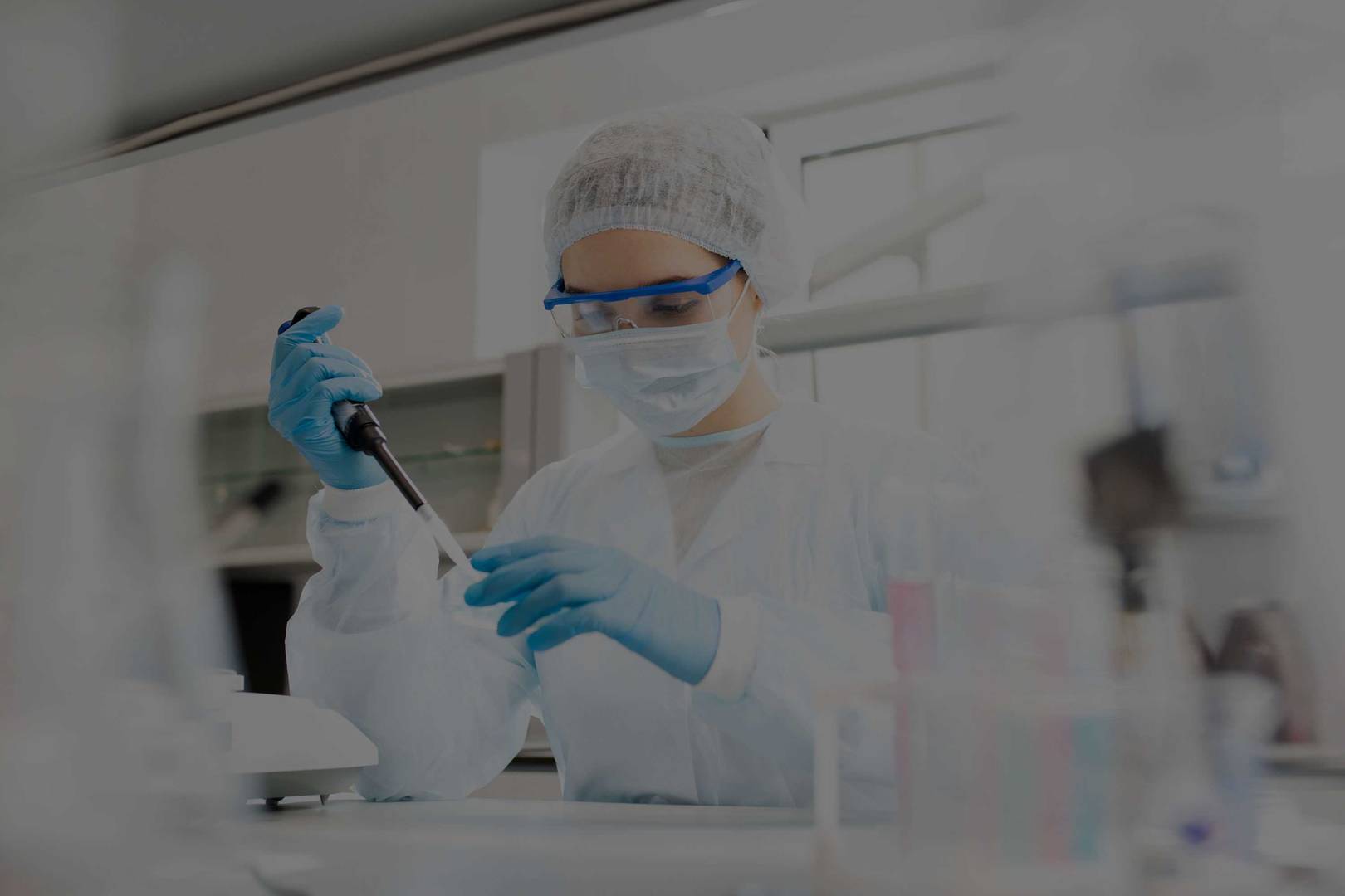 Microbiologist in sterile clothing and safety goggles adding reagent to a petri dish in a laboratory