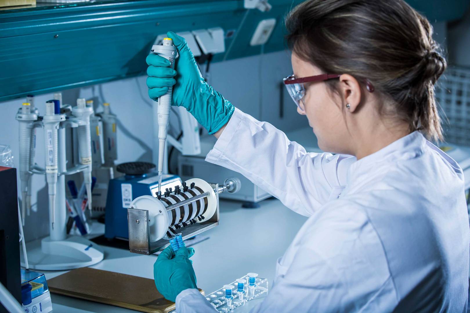 A scientist in a lab coat examines two vials while using a micropipette for precise liquid measurement.