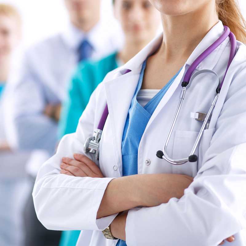 A group of medical professionals in white coats and scrubs, with a close-up focus on a female doctor crossing her arms.